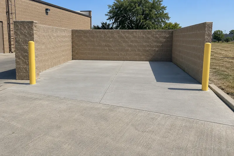 Commercial Concrete in McGregor, TX, example photo: new concrete dumpster pad with bollards behind a small commercial building