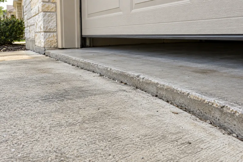 Concrete Contractor in Crawford, TX, example photo: a driveway panel sunk at the garage door, leaving a raised trip edge