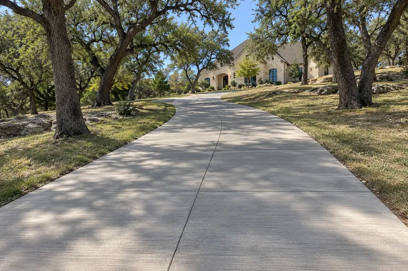 Concrete Contractor in Woodway, TX, example photo: long new concrete driveway to a stone home on a wooded lot